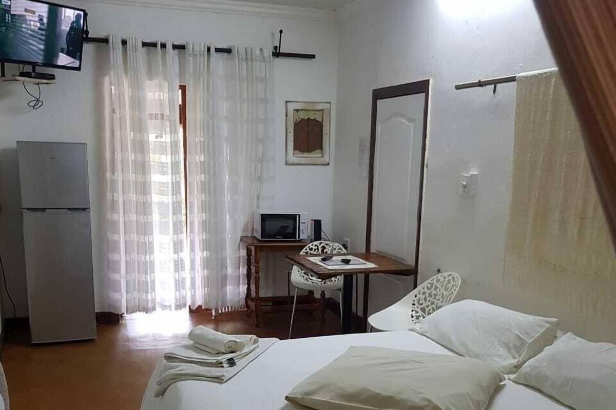 A hotel room with a bed, a desk, a television, and a refrigerator.