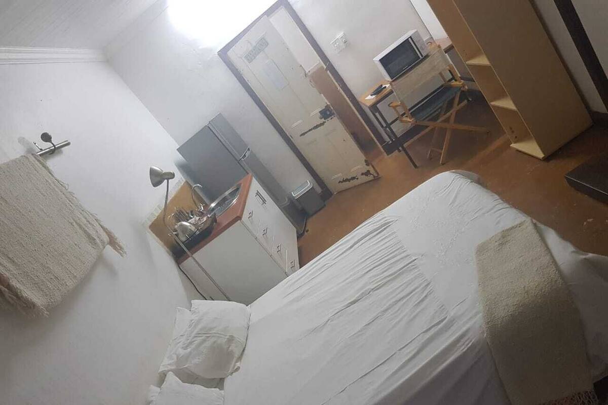 A small, sparsely furnished room with a bed, a desk, and a chair.
