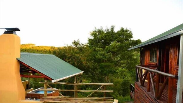 A rustic cabin with a green roof, a wooden deck, and a hot tub. - Mulberry Lane Suites (Graskop)