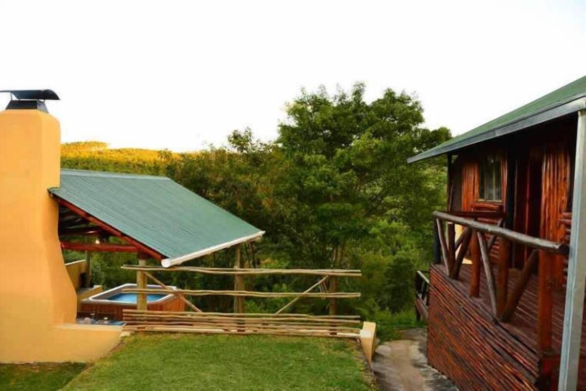 A rustic cabin with a green roof, a wooden deck, and a hot tub.