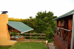 A rustic cabin with a green roof, a wooden deck, and a hot tub. - Mulberry Lane Suites (Graskop)
