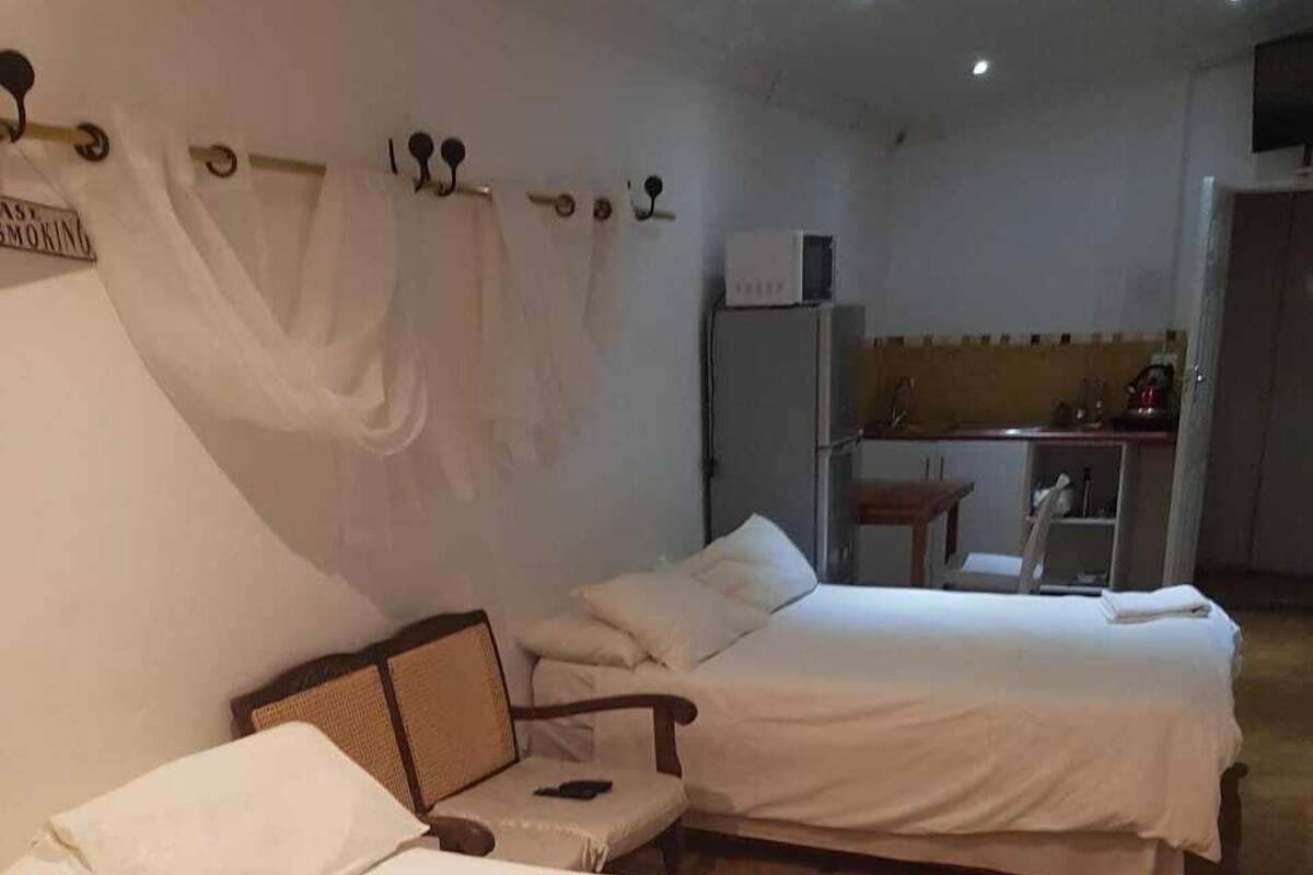 Two single beds with white linens, a small wooden chair, and a kitchenette area in the background.