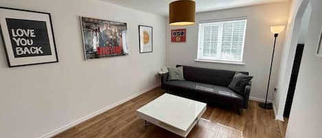 Una sala de estar moderna con un sofá negro, una mesa de centro blanca y carteles enmarcados en la pared.