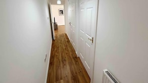 Ein Korridor mit Holzboden, weißen Wänden und einer Deckenleuchte.