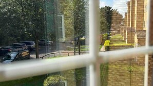 Blick aus einem Fenster auf einen Parkplatz mit Autos, eine Kreisverkehr und ein Gebäude mit Backsteinfassade.