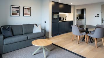 Un salon moderne avec un canapé gris, une table basse ronde en bois et un coin repas comprenant des chaises grises et une table noire.