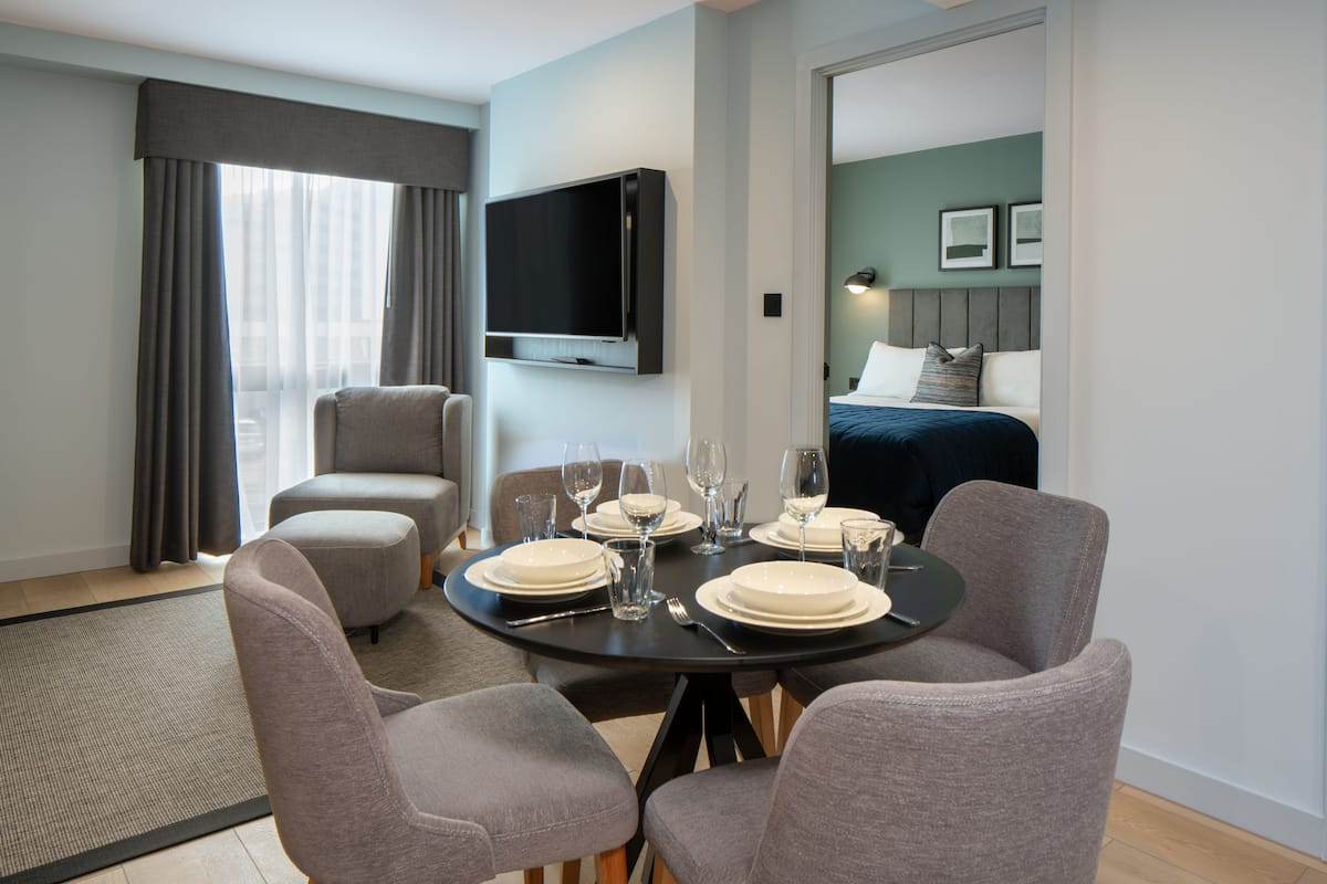 Ein Hotelzimmer mit Essbereich, einem Bett, einem Fernseher und Blick auf die Stadt.