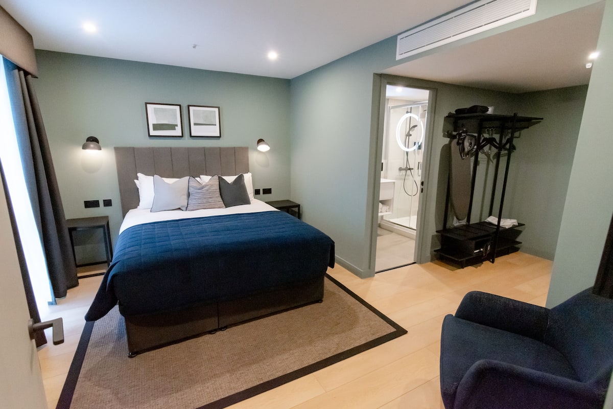 Ein modernes Hotelzimmer mit einem großen Bett, Nachttischen, einer Sitzecke und einem Duschbereich.