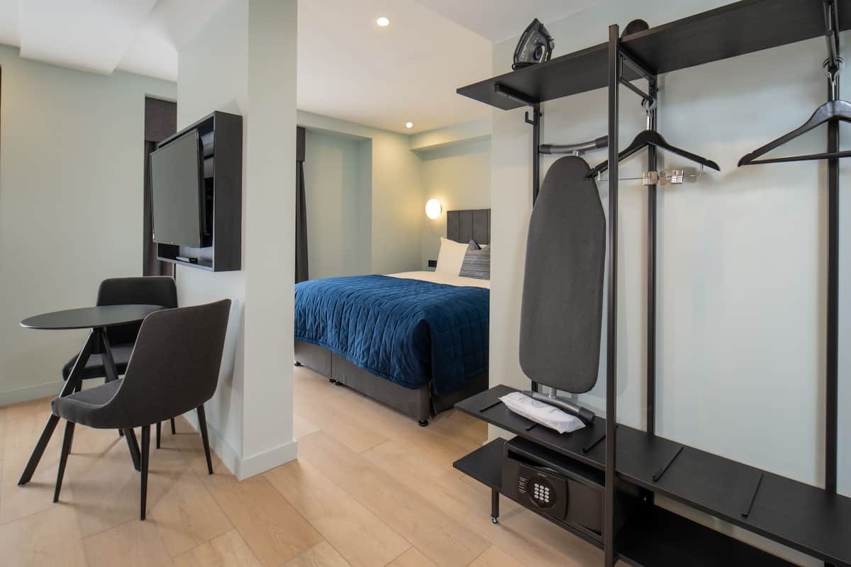 Ein modernes Hotelzimmer mit Bett, Schreibtisch, Stuhl, Fernseher und Kleiderschrank.