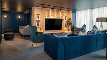 Un salon moderne avec un grand téléviseur à écran plat, un canapé bleu, un fauteuil vert et une lampe sur pied.