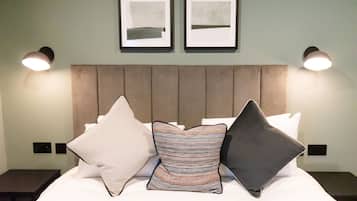 A neatly made bed with a headboard, two framed artworks on the wall, and two bedside lamps.