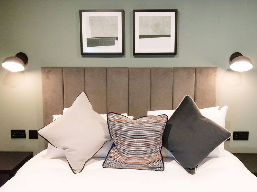 A neatly made bed with a headboard, two framed artworks on the wall, and two bedside lamps.