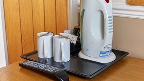 A coffee maker, two mugs, and a remote control on a tray.