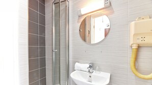 A bathroom with a glass shower enclosure, a white sink, and a round mirror.