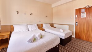 A hotel room with two beds, a wooden door, a nightstand, and a radiator.