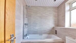 A modern bathroom with a glass-enclosed shower, a white bathtub, and a toilet.