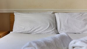 A neatly made bed with white linens and pillows, a wooden nightstand, and a rolled white towel. - Properties Unique / Dene Rooms Family 35 (Newcastle Upon Tyne)