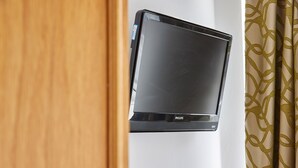 A wall-mounted flat-screen TV with a Philips logo, a wooden door frame, and a patterned curtain. - Properties Unique | Dene Rooms Single 38 (Newcastle Upon Tyne)