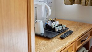 A kitchenette with a coffee maker, a tray with cups and condiments, a remote control, and a microwave. - Properties Unique | Dene Rooms Single 38 (Newcastle Upon Tyne)