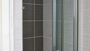 A modern bathroom with dark tiled walls, a glass shower enclosure, and a metallic faucet. - Properties Unique | Dene Rooms Single 38 (Newcastle Upon Tyne)