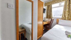 A hotel room with a bed, a desk, a chair, a television, and a window with curtains. - Properties Unique | Dene Rooms Single 38 (Newcastle Upon Tyne)