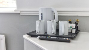A tray with mugs, a coffee pot, and a remote control on a white counter near a window. - Properties Unique | Dene Rooms Triple 29 (Newcastle Upon Tyne)
