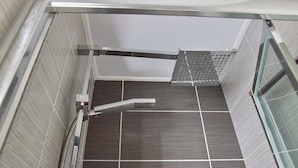 Une douche avec une porte en verre, une poignée en métal et un sol carrelé.