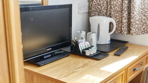 Un bureau en bois, un téléviseur à écran plat, une machine à café, une télécommande et un plateau avec des tasses et des condiments.