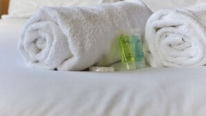 Een keurig opgerolde witte handdoek, een klein flesje lotion en een tube crème op een bed.