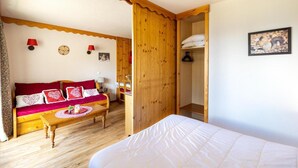 Una camera accogliente con pavimento in legno, un divano rosso con cuscini a motivi floreali e un letto bianco, oltre a un armadio in legno.