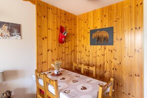 A dining area with a wooden wall, a table with heart-patterned tablecloths, and a vase with flowers.