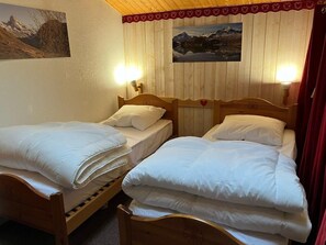 Cozy bedroom with two beds, each with a white duvet and pillow, and a wall-mounted picture of a mountainous landscape.