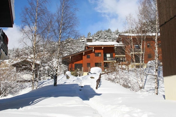 A snow-covered landscape with a red building featuring multiple balconies and a wooden structure in the foreground.