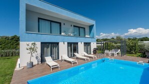 A modern two-story building with a swimming pool, outdoor seating, and a well-maintained garden.