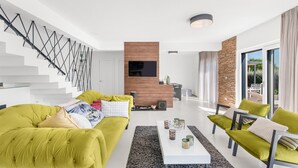 A modern living room with a staircase, a flat-screen TV, and a stone accent wall.