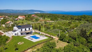 A modern house with a swimming pool, surrounded by lush greenery and a scenic view of the sea.