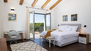 A bedroom with a bed, a desk, a chair, a nightstand, and a balcony with a view.