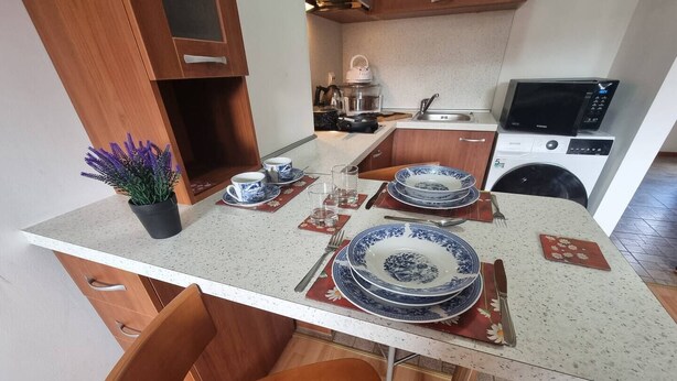 A compact kitchen with wooden cabinets, a microwave, and a sink. - 1BR Homey Duplex 300mbps Wifi 2 Floor With Washer (Bansko)
