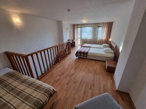 Ein Zimmer mit zwei Betten, Holzboden, einem Balkon mit Geländer und einem Vorhangfenster.