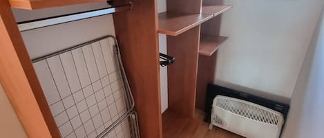 Quarto pequeno com um guarda-roupa de madeira, um radiador e uma janela.