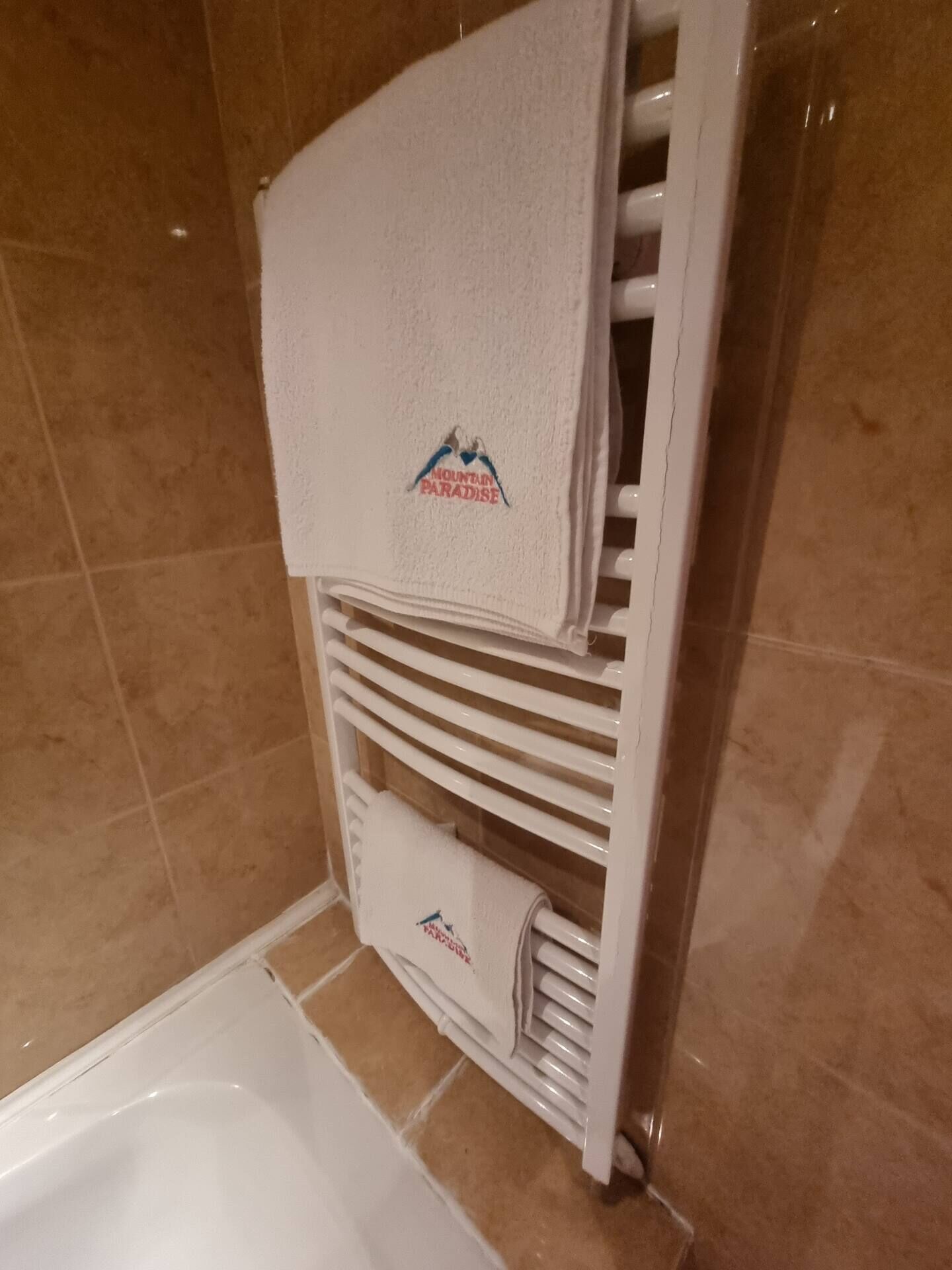 A bathroom with a white towel rack holding several towels, one of which has a logo.