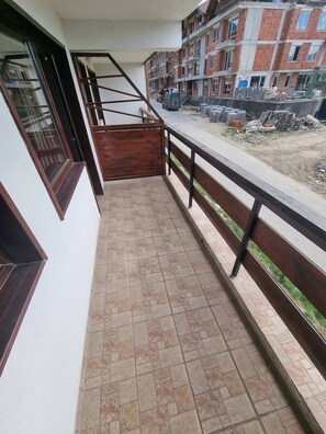 Un balcon avec un sol carrelé, une rambarde en bois et une vue sur un chantier de construction.