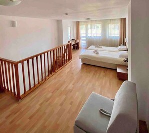 A hotel room with a wooden floor, a bed, a sofa, and a balcony with a wooden railing.