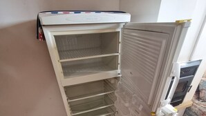 Un coin de pièce avec un réfrigérateur blanc, un plancher en bois et une vue partielle d’un canapé.