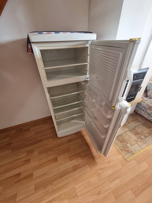 Un coin de pièce avec un réfrigérateur blanc, un plancher en bois et une vue partielle d’un canapé.
