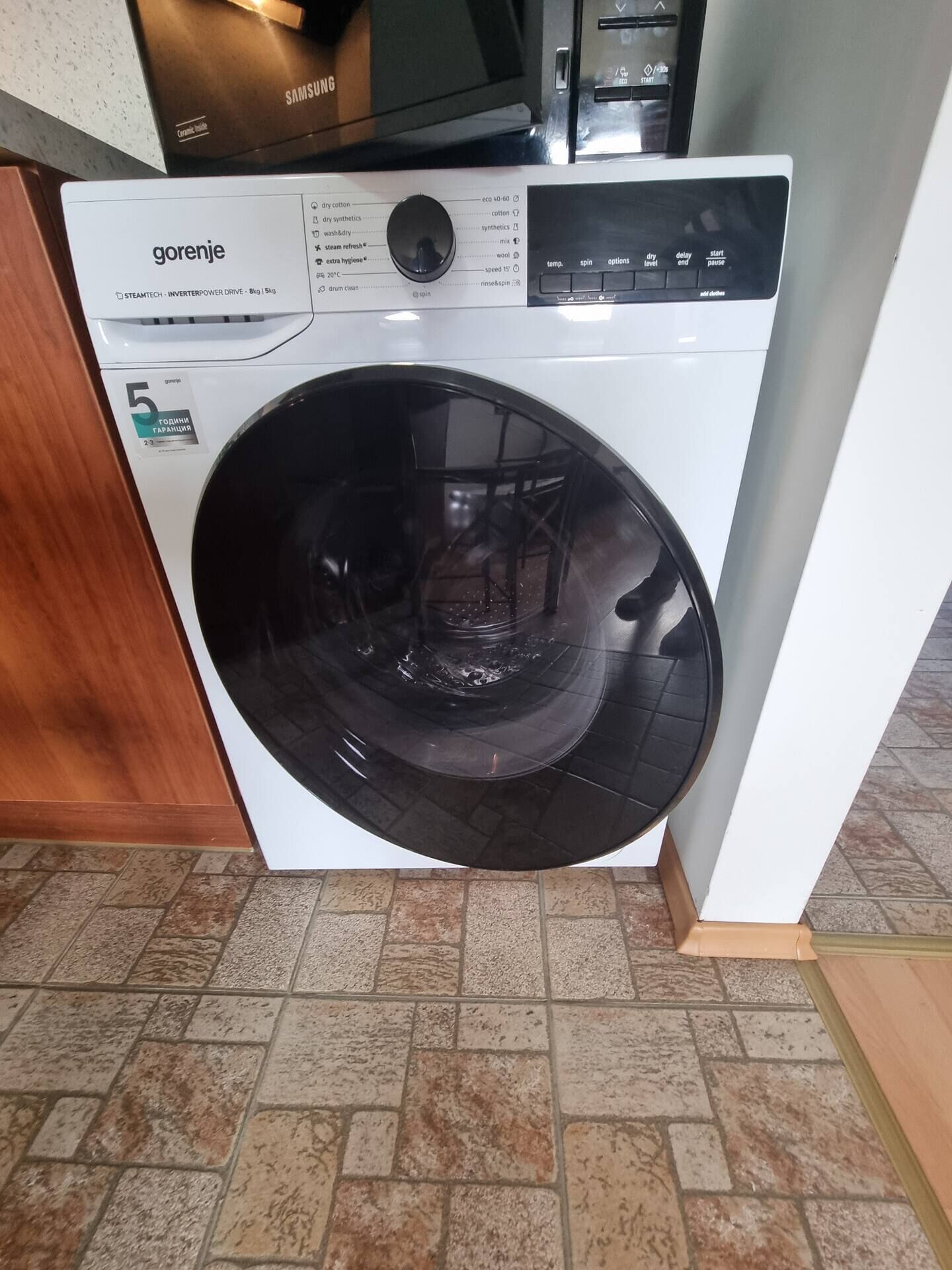 A front-loading white washing machine with a control panel, a label indicating it is a 5-gallon capacity model, and a price tag of 23.