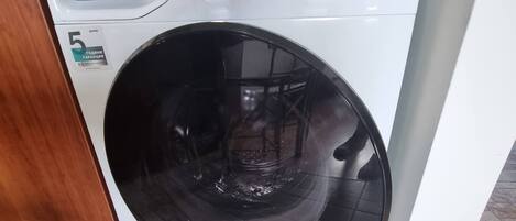 A front-loading white washing machine with a control panel, a label indicating it is a 5-gallon capacity model, and a price tag of 23.