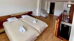 Une chambre d’hôtel avec deux lits, un plancher en bois, un petit coin salon et un escalier.