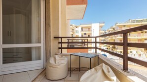 Un balcón con puerta corredera de vidrio, una mesita, un sillón tipo bean bag y vistas a edificios cercanos.