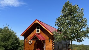 Una cabaña de troncos con techo rojo, un porche delantero y una terraza de madera.